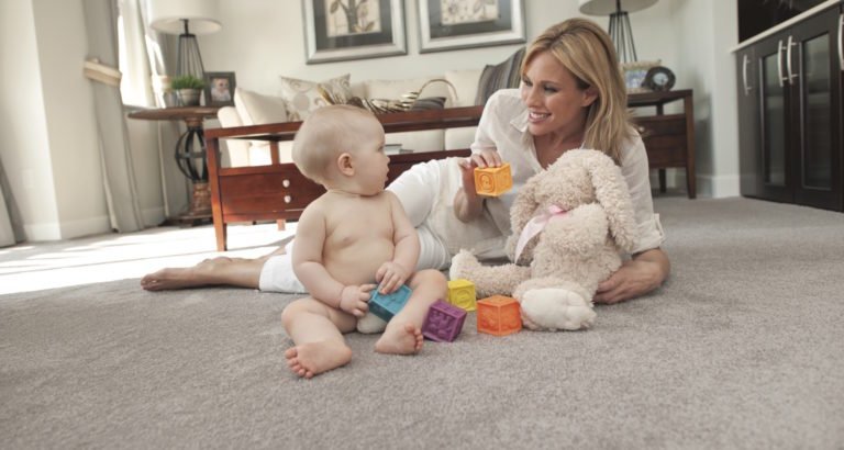 Mother playing with baby on carpet flooring